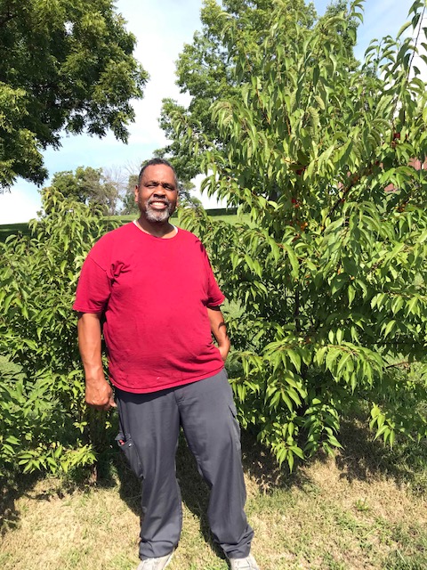 Man in red shirt standing with tree.